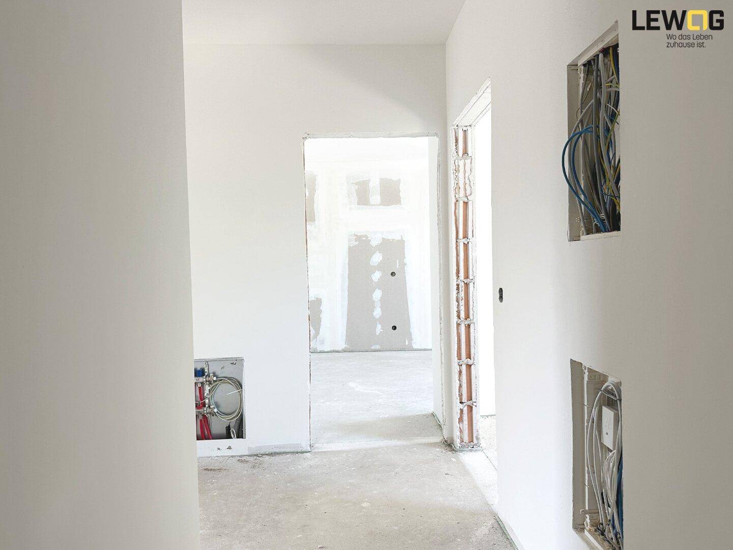 Unfertiger Innenraum mit sichtbaren Installationen und Rohbauwänden.