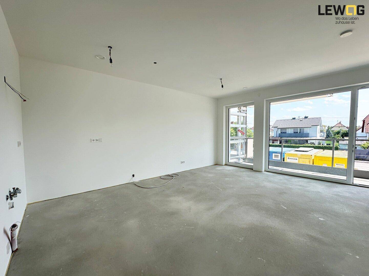Unfertiger Wohnbereich mit großen Fenstern und Blick auf die Baustelle, bereit für den Innenausbau.