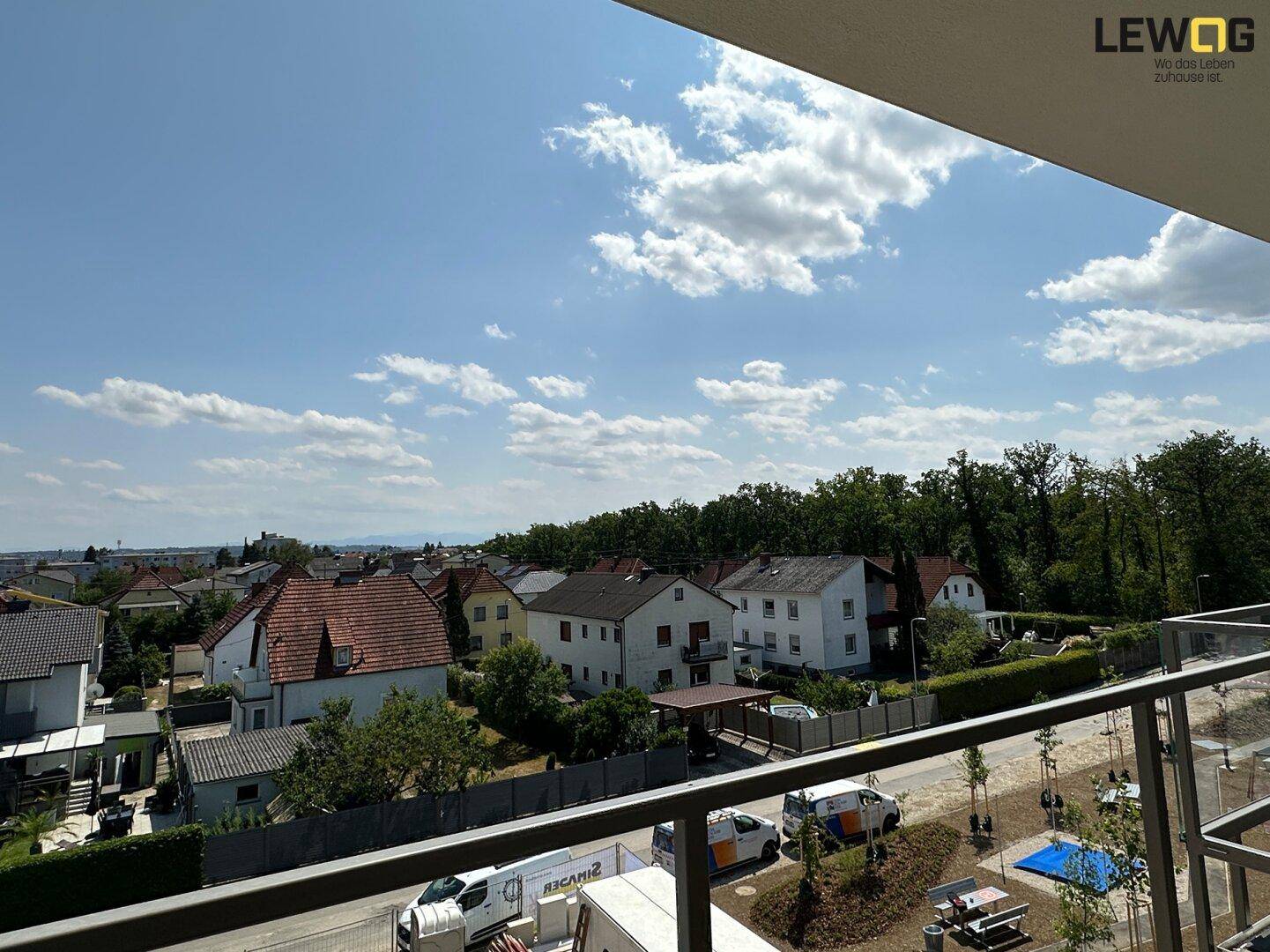 Weitläufiger Blick von einem Balkon über eine Wohnsiedlung und grüne Baumreihen.