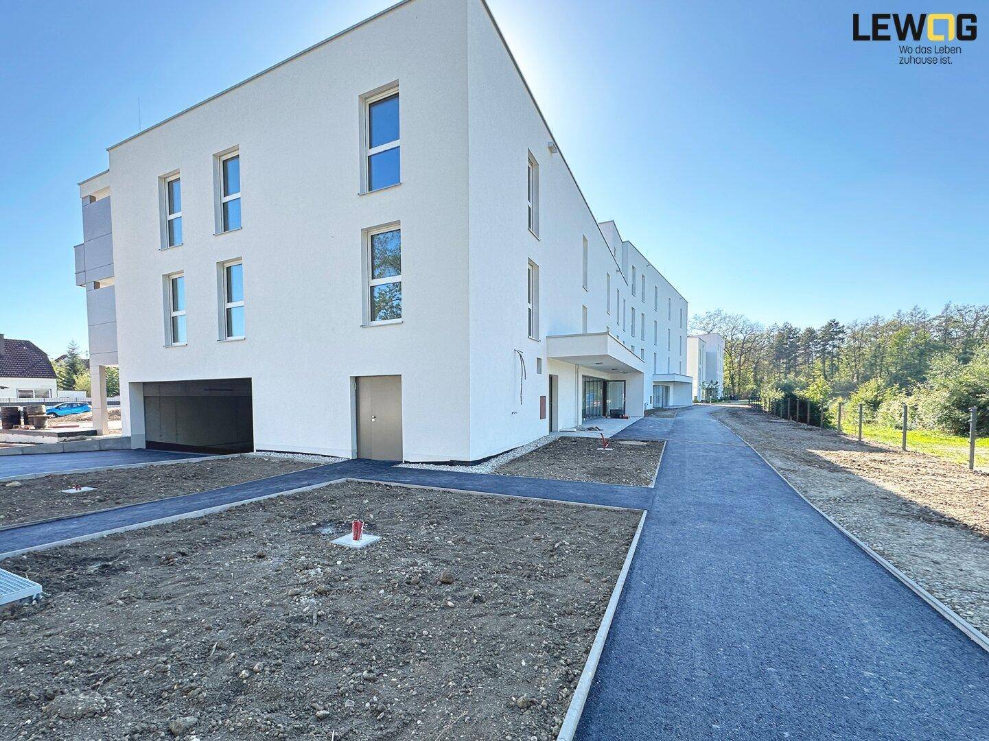 Seitenansicht des Neubaus mit Eingangsbereich, Fenstern und vorbereiteter Außenanlage.
