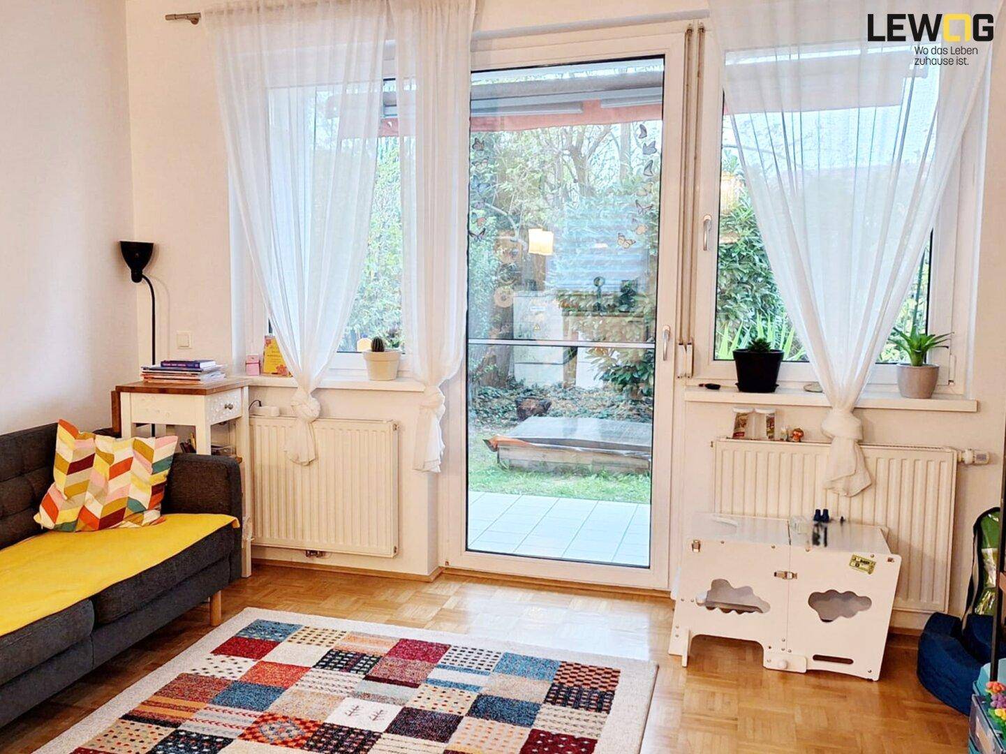 Gemütliches Wohnzimmer mit Holzboden, farbenfrohem Teppich und direktem Zugang zum Garten.