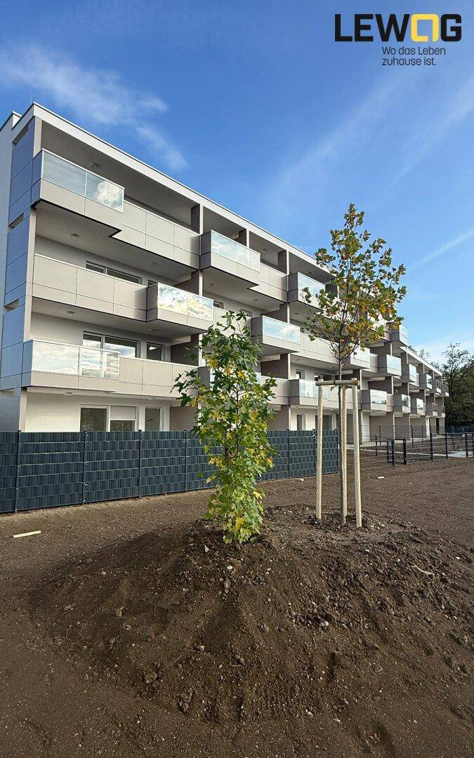 Neubau mit moderner Architektur, Balkonen und vorbereiteten Grünflächen unter klarem Himmel.