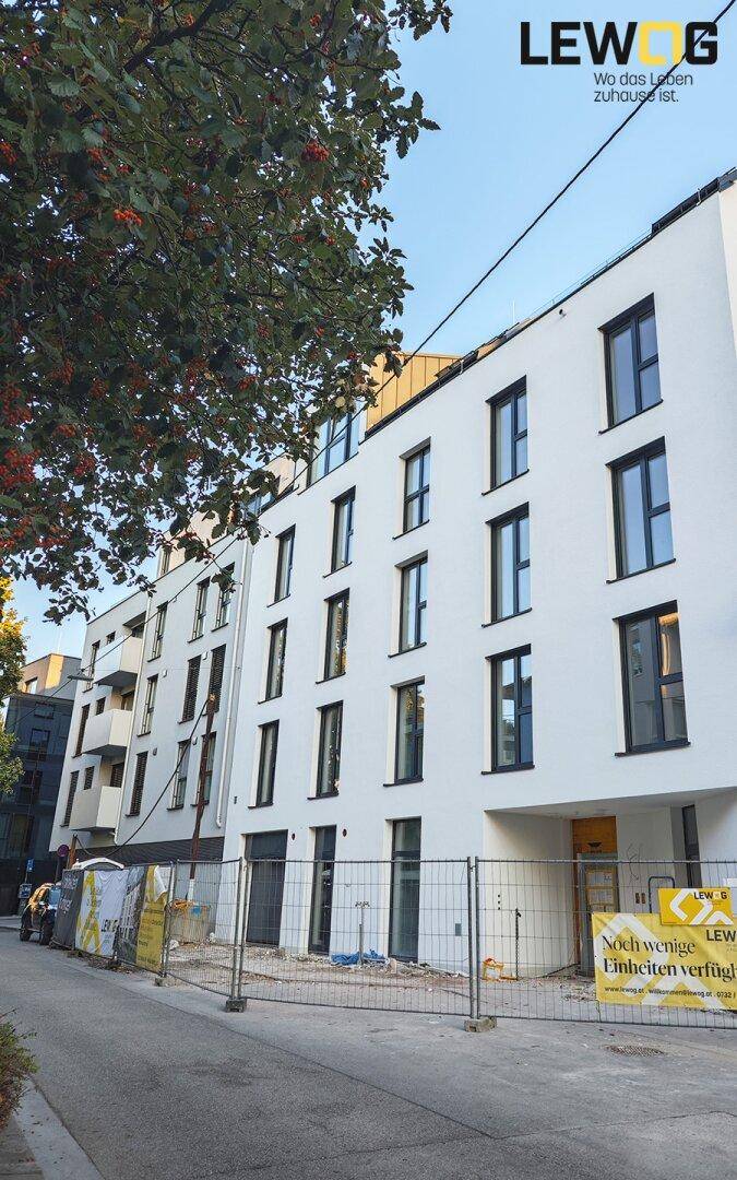 Moderne Wohngebäude mit weißer Fassade und dunklen Fenstern, umgeben von Bauzäunen.