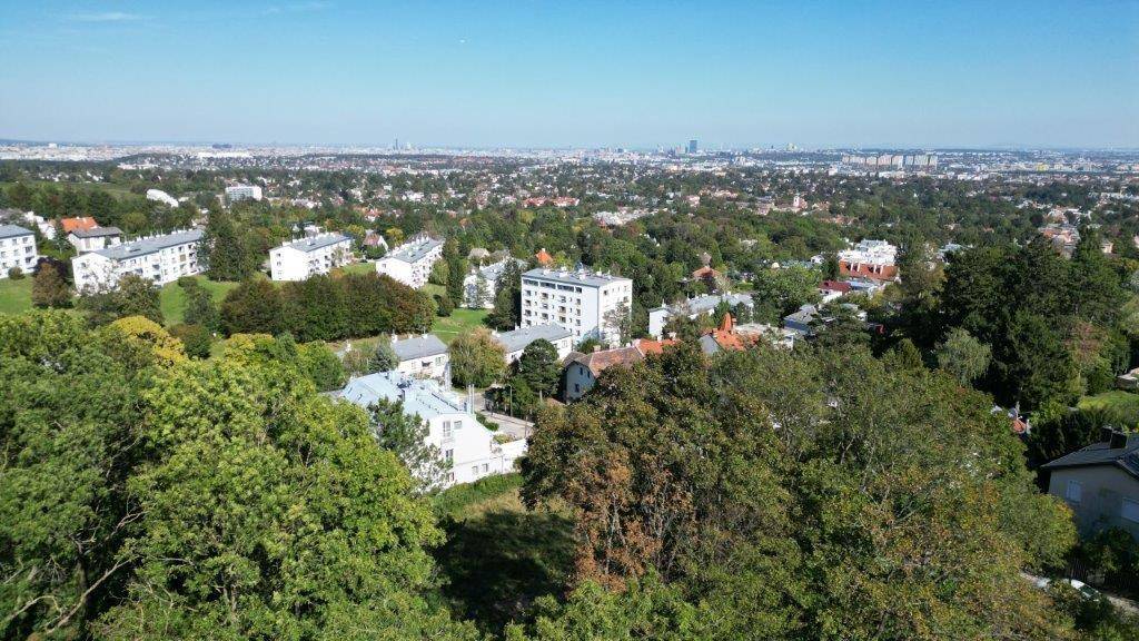 Panoramablick über eine grüne Vorstadtlandschaft mit Gebäuden und Stadtsilhouette am Horizont.