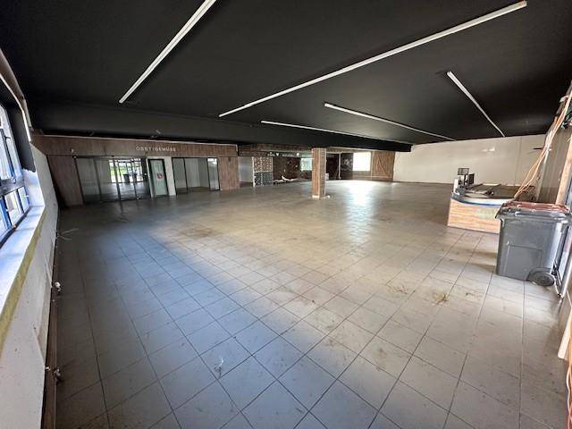 Geräumiger, leerer Verkaufsraum mit Fliesenboden, dunkler Decke und Eingangsbereich mit Glastüren und Theke.