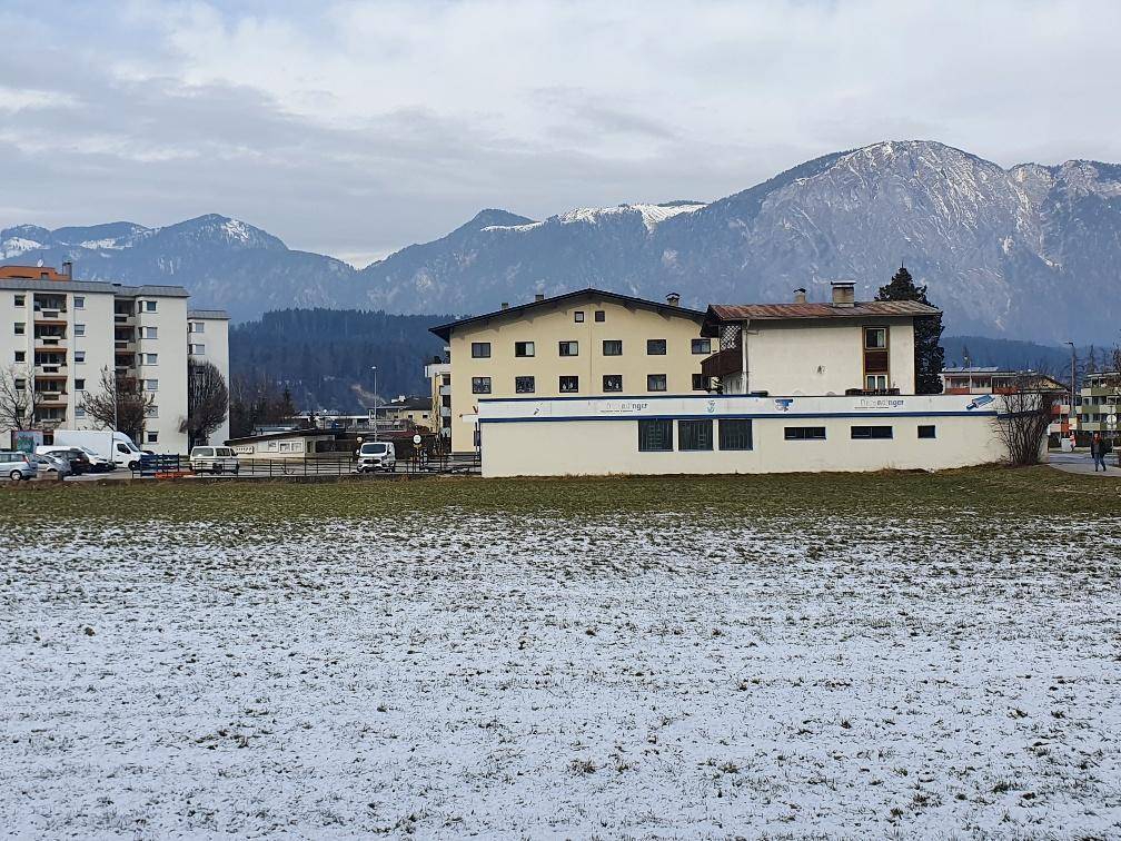 Winterliche Außenansicht des Gewerbegebäudes mit schneebedecktem Feld und imposanter Bergkulisse im Hintergrund.