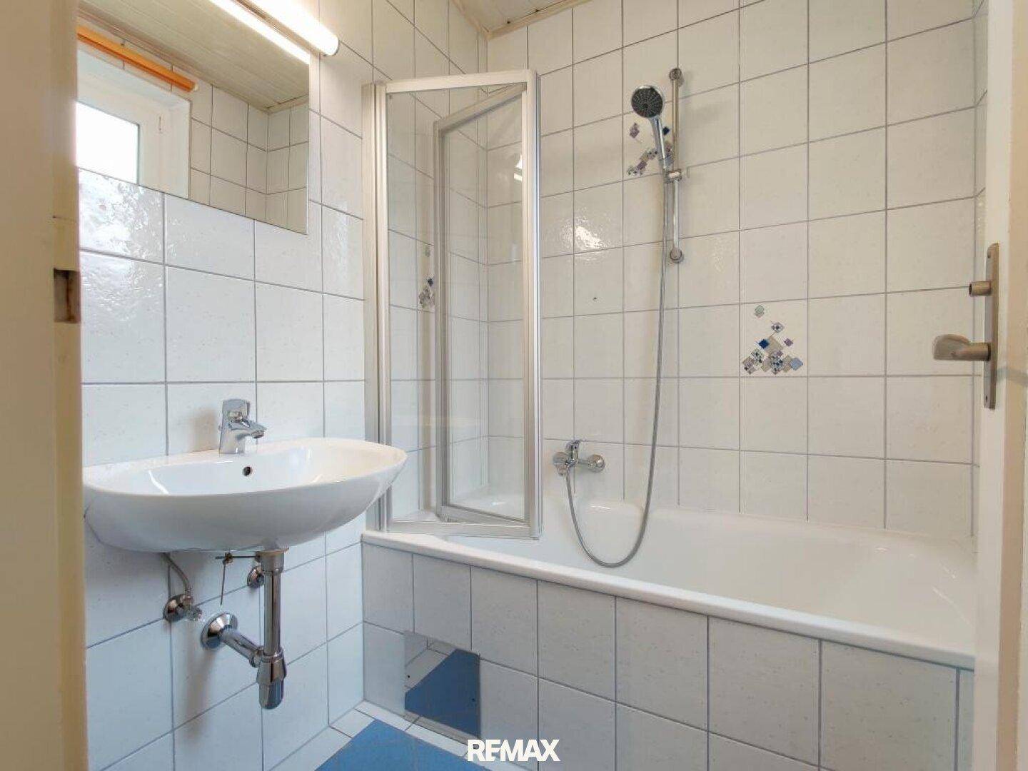 Badezimmer mit Badewanne, Duschabtrennung und weißen Fliesen.