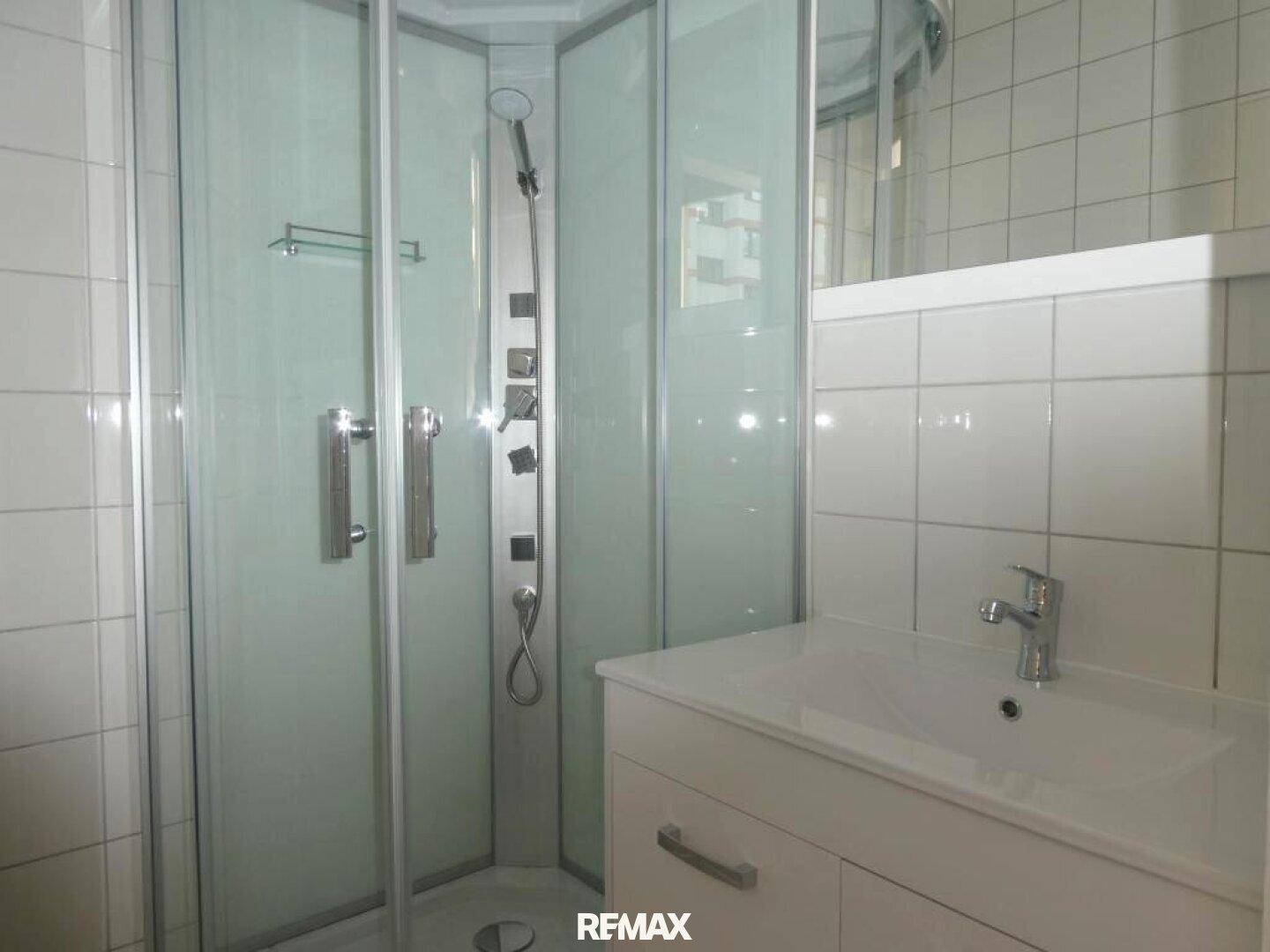 Badezimmer mit Eckduschkabine, modernem Waschtisch und weißen Fliesen an den Wänden.