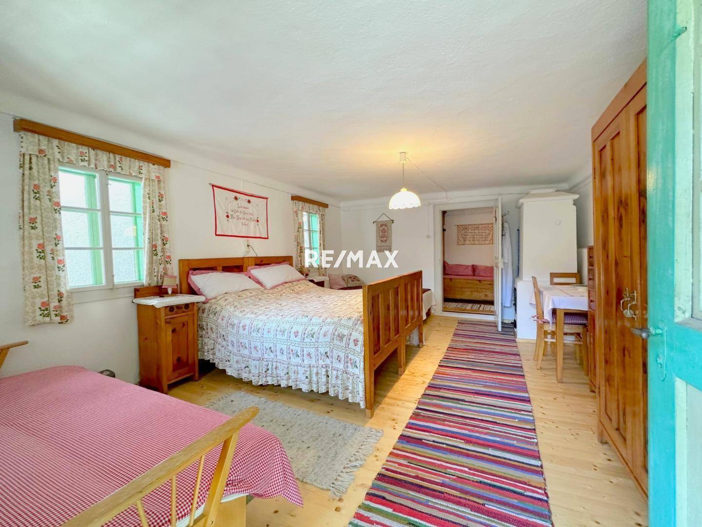 Geräumiges Schlafzimmer mit zwei Betten, Holzboden und farbenfrohen Teppichen, mit Zugang zu einem weiteren Raum.