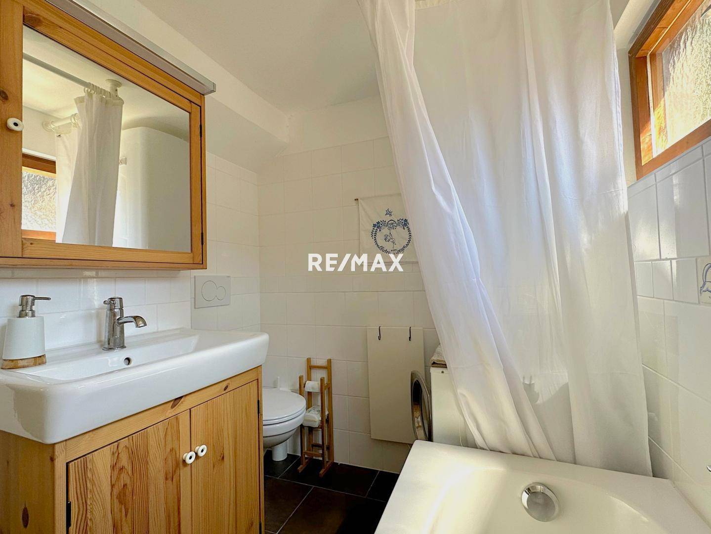 Helles Badezimmer mit Badewanne, Waschbecken und Holzunterschrank, weiß gefliest.