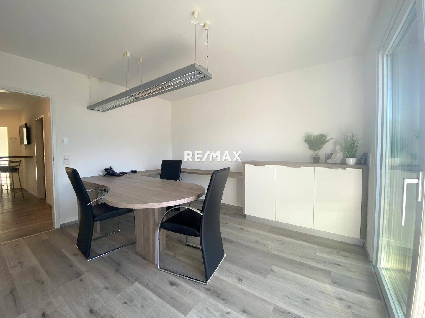 Heller Raum mit modernem Holztisch, schwarzen Stühlen und einem Sideboard, ideal als Büro oder Essbereich.