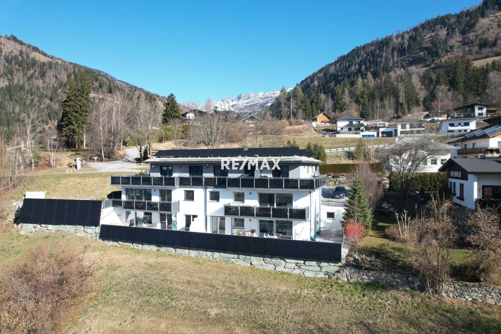 Weitläufige Ansicht eines modernen Apartmentgebäudes mit Balkonen und Solaranlagen in einer Berglandschaft.