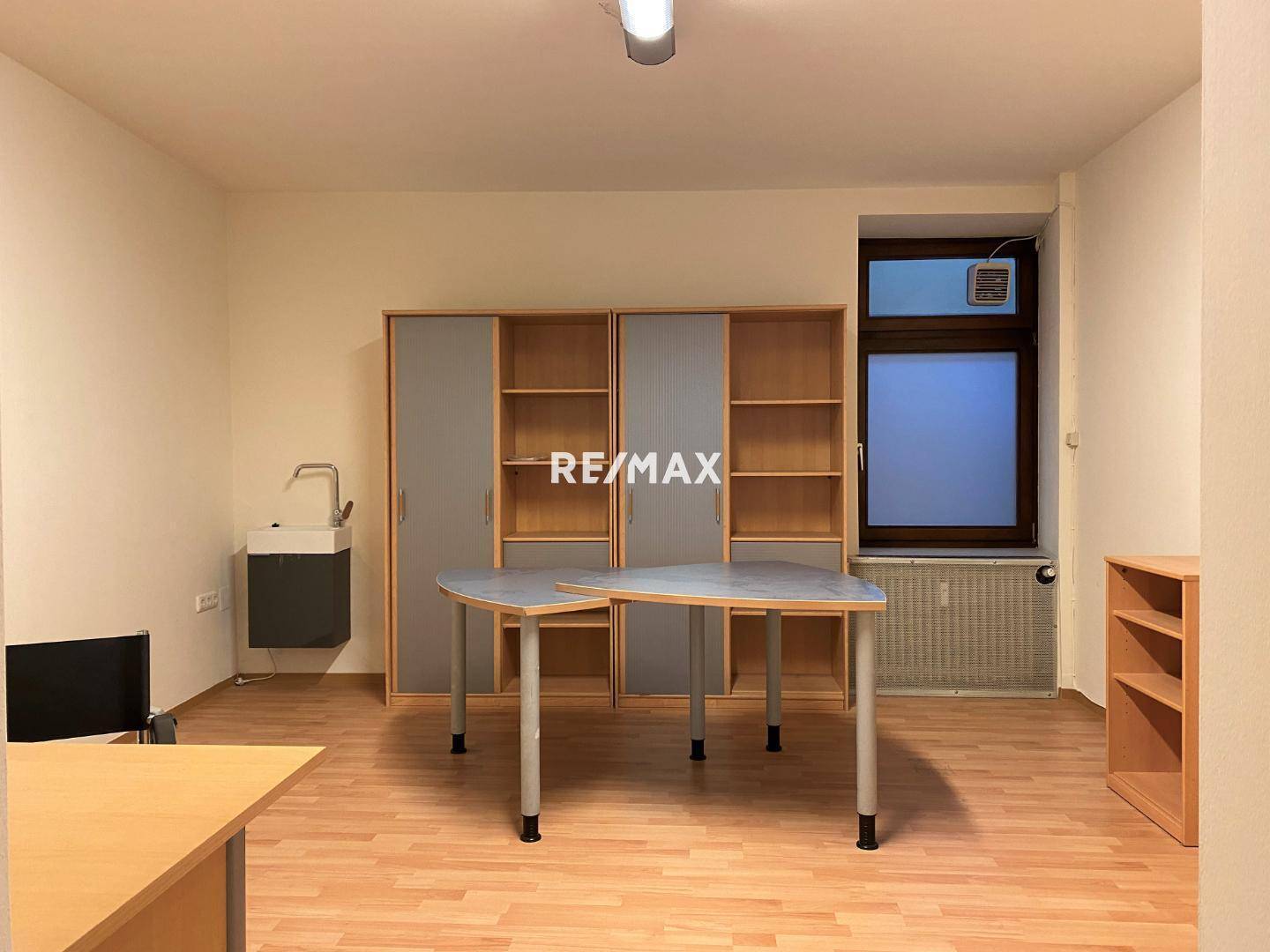 Funktionaler Arbeitsraum mit Laminatboden, Einbauschränken, einem Waschbecken und einem Fenster mit Heizkörper.