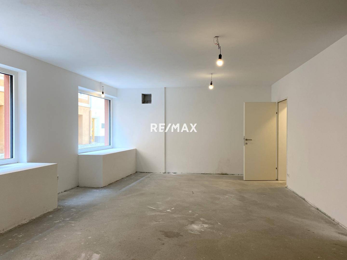 Großer, leerer Raum mit Betonboden und großen Fenstern, ideal für den Ausbau.