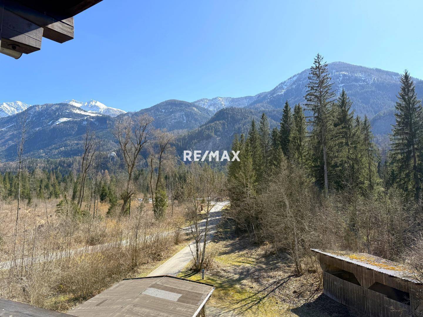 Weitläufiger Blick auf bewaldete Berge und eine ländliche Umgebung unter strahlend blauem Himmel.