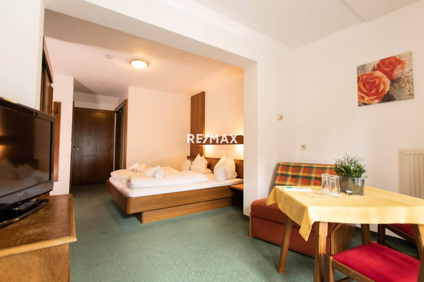 Gemütliches Schlafzimmer mit Doppelbett, grünem Teppichboden und einem kleinen Esstisch für zwei Personen.