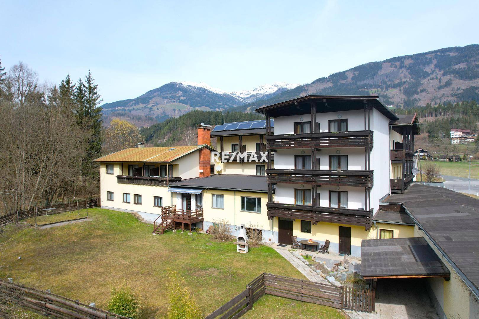 Rückseite des Hotels mit mehreren Balkonen, einem gepflegten Gartenbereich und Solarpaneelen auf dem Dach.