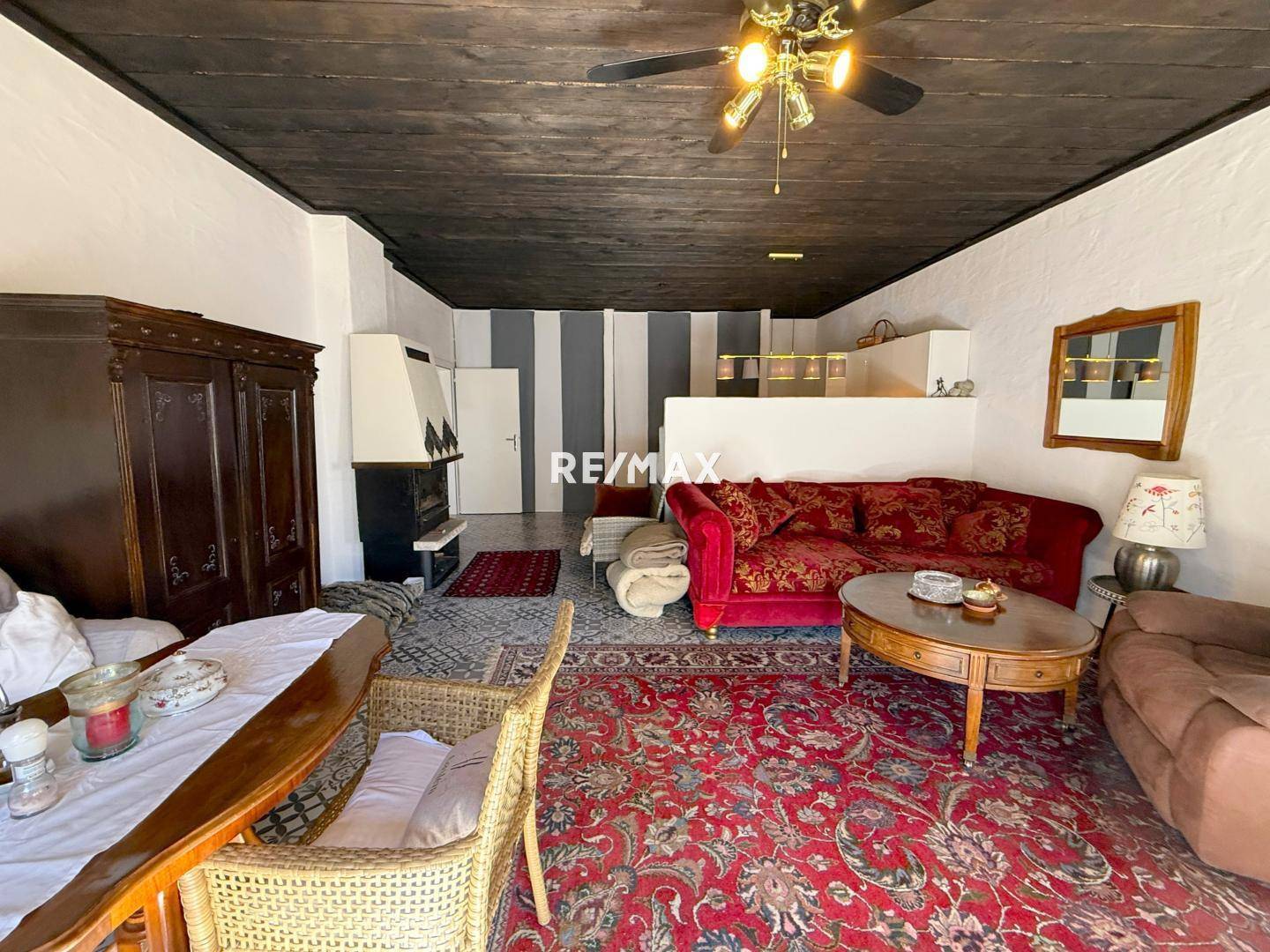 Geräumiger Wohnbereich mit rotem Teppich, Kamin und einer markanten dunklen Holzbalkendecke.