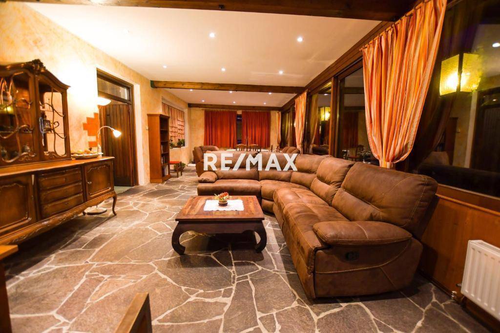 Gemütlicher Wohnbereich mit großem braunem Ecksofa, rustikalem Steinfliesenboden und Holzbalkendecke.