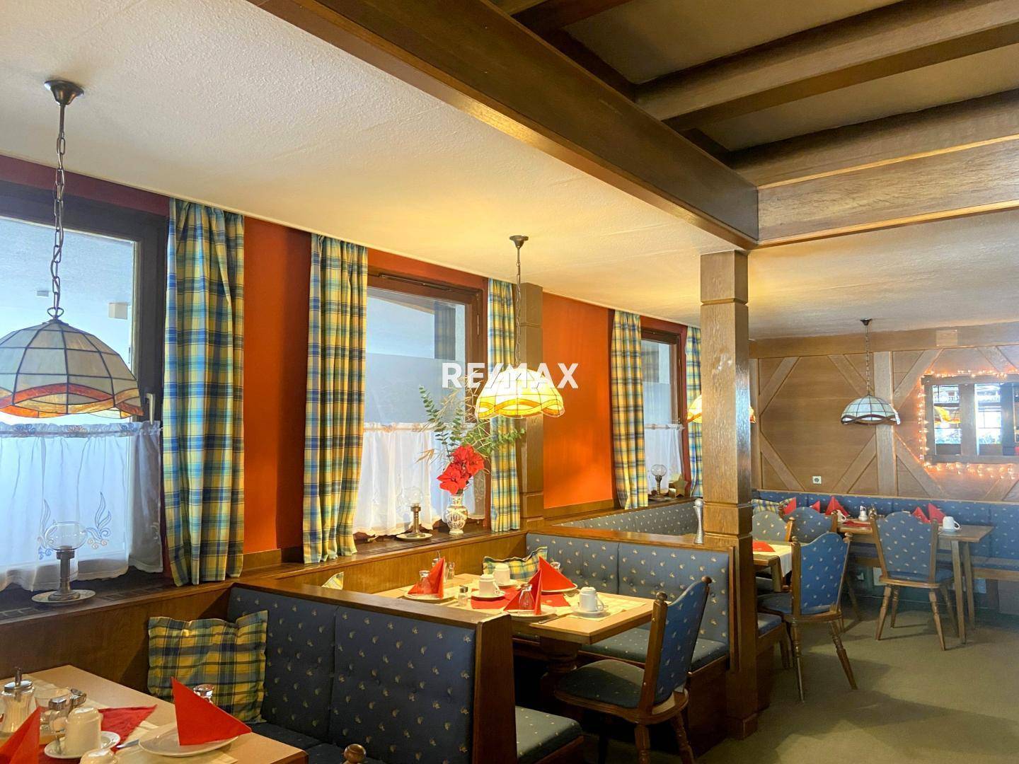 Gemütlicher Restaurantbereich mit karierten Vorhängen, Holztischen und blauen Sitzbänken, hell und einladend.