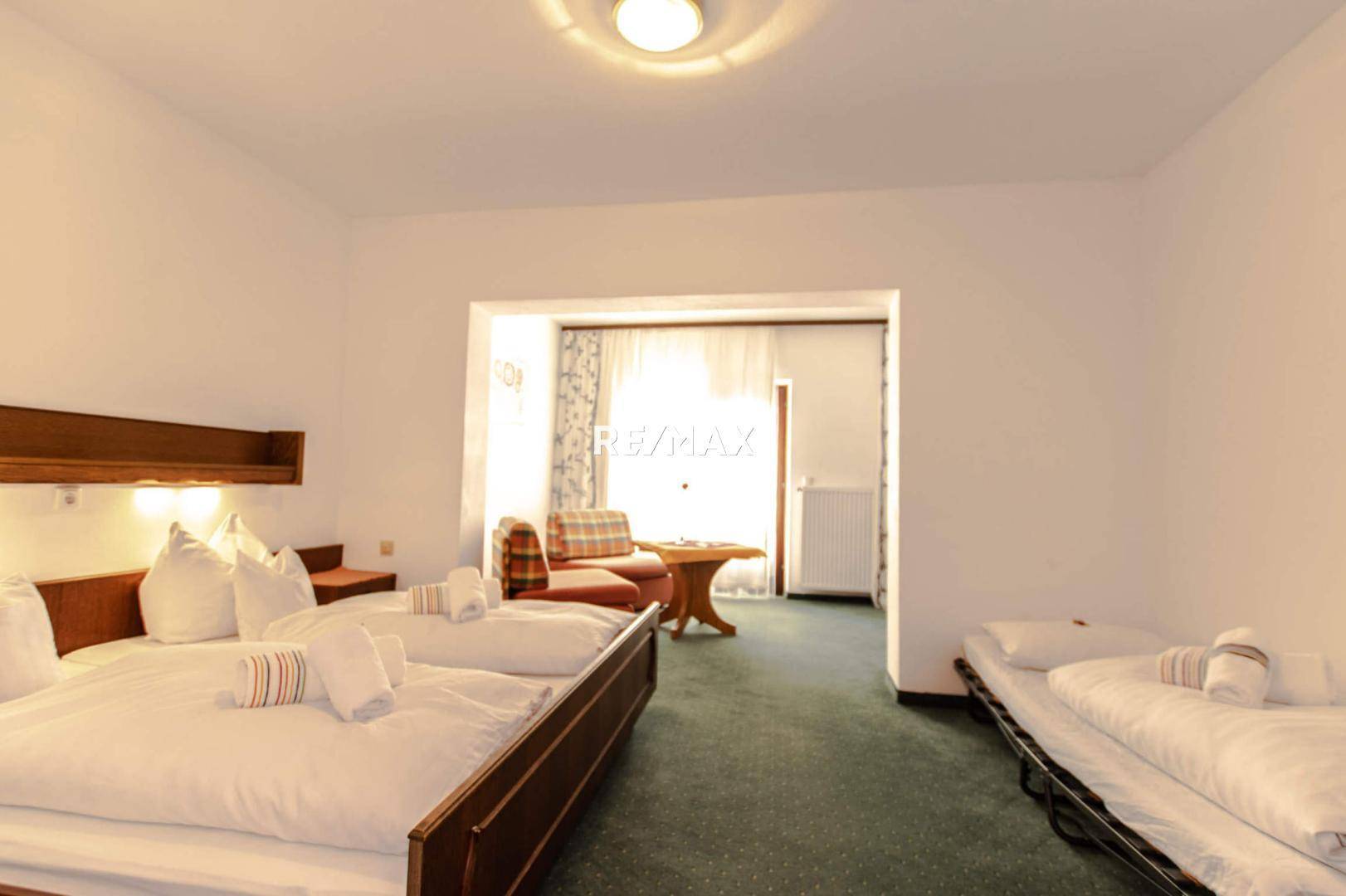 Helles Schlafzimmer mit zwei Betten, grünem Teppichboden und einem separaten, gemütlichen Sitzbereich.