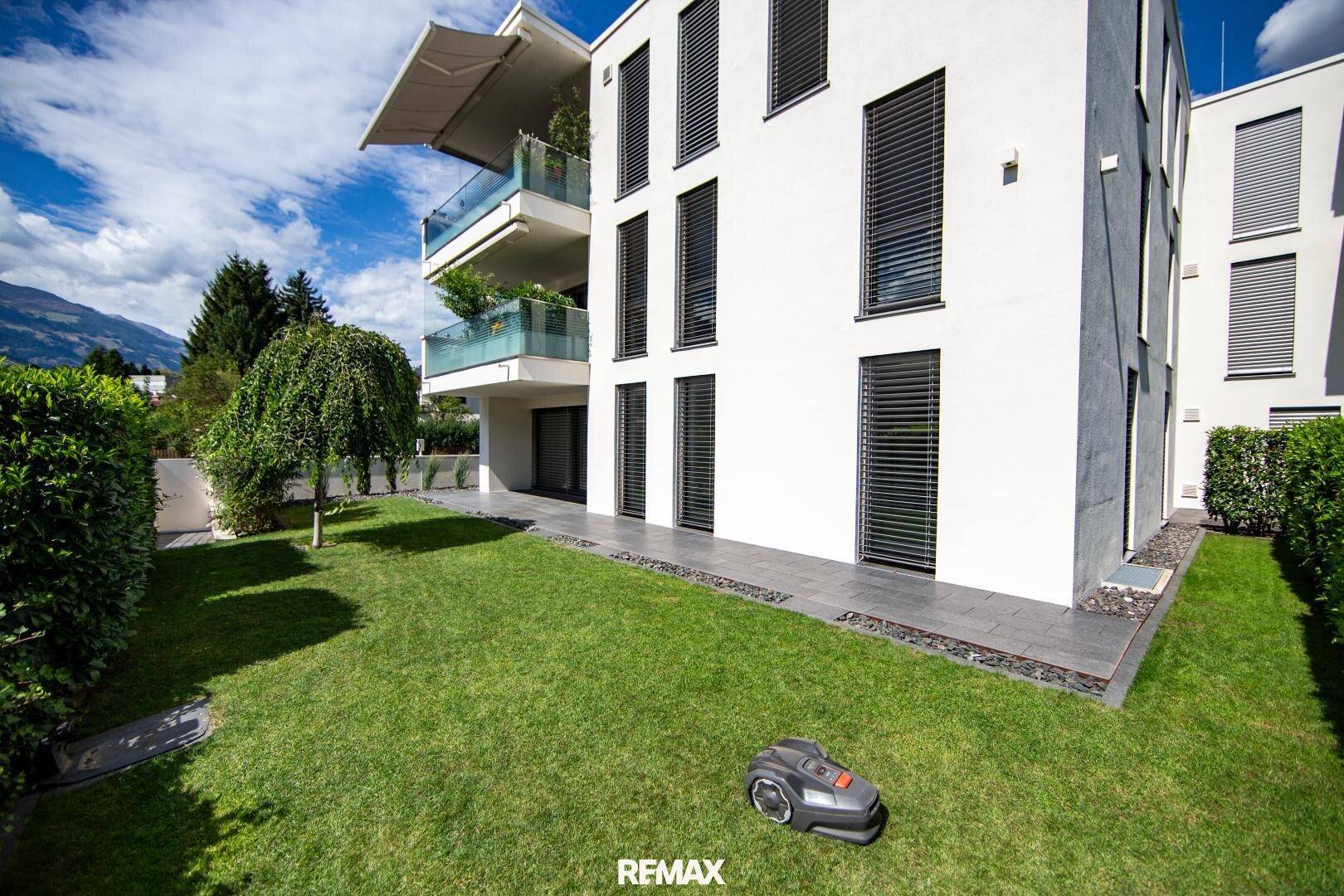 Gepflegter Rasen mit Mähroboter und moderner Terrasse am Erdgeschoss eines Neubaus.