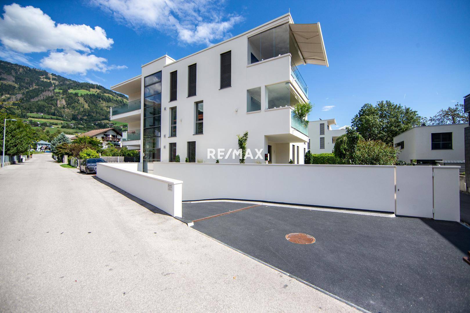 Moderne Wohnanlage mit Zufahrt zur Tiefgarage und Bergblick.