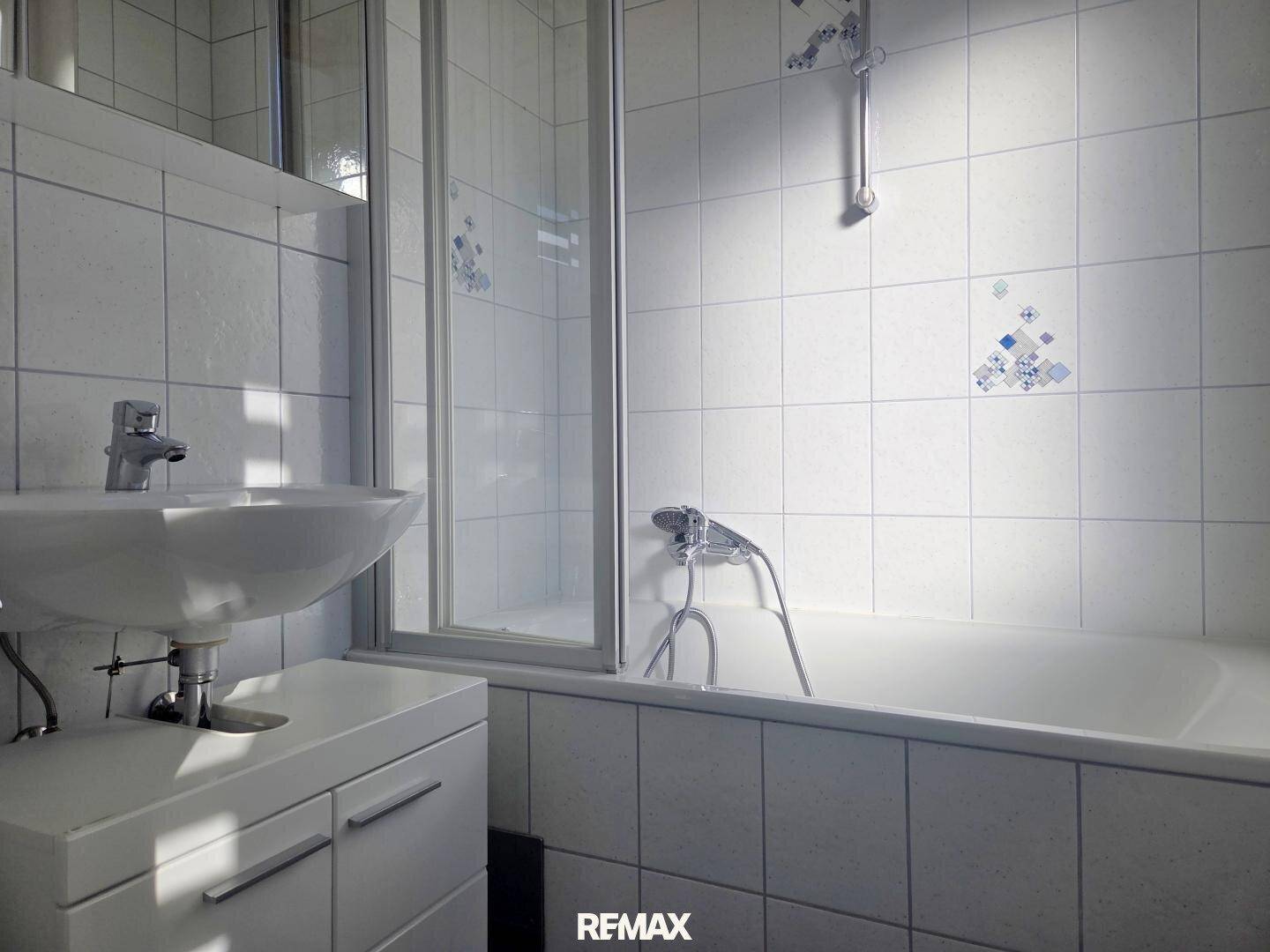 Badezimmer mit Badewanne, Duschabtrennung, Waschbecken und Spiegelschrank.