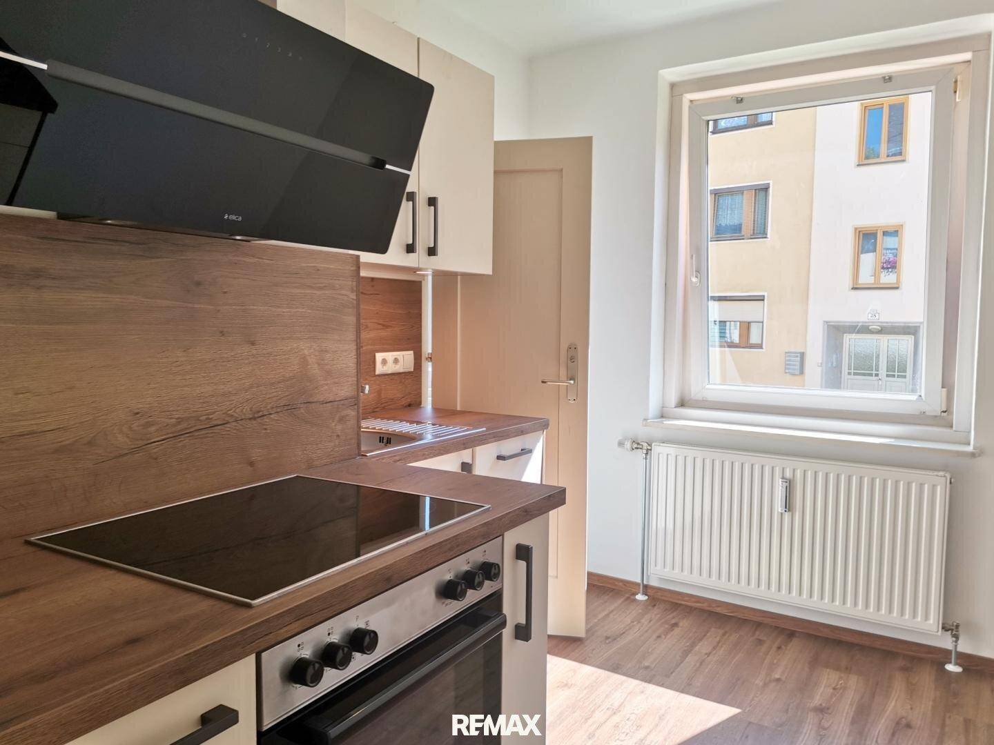 Moderne Küche mit Induktionskochfeld, Backofen und Holz-Arbeitsplatten, hell durch Fenster.