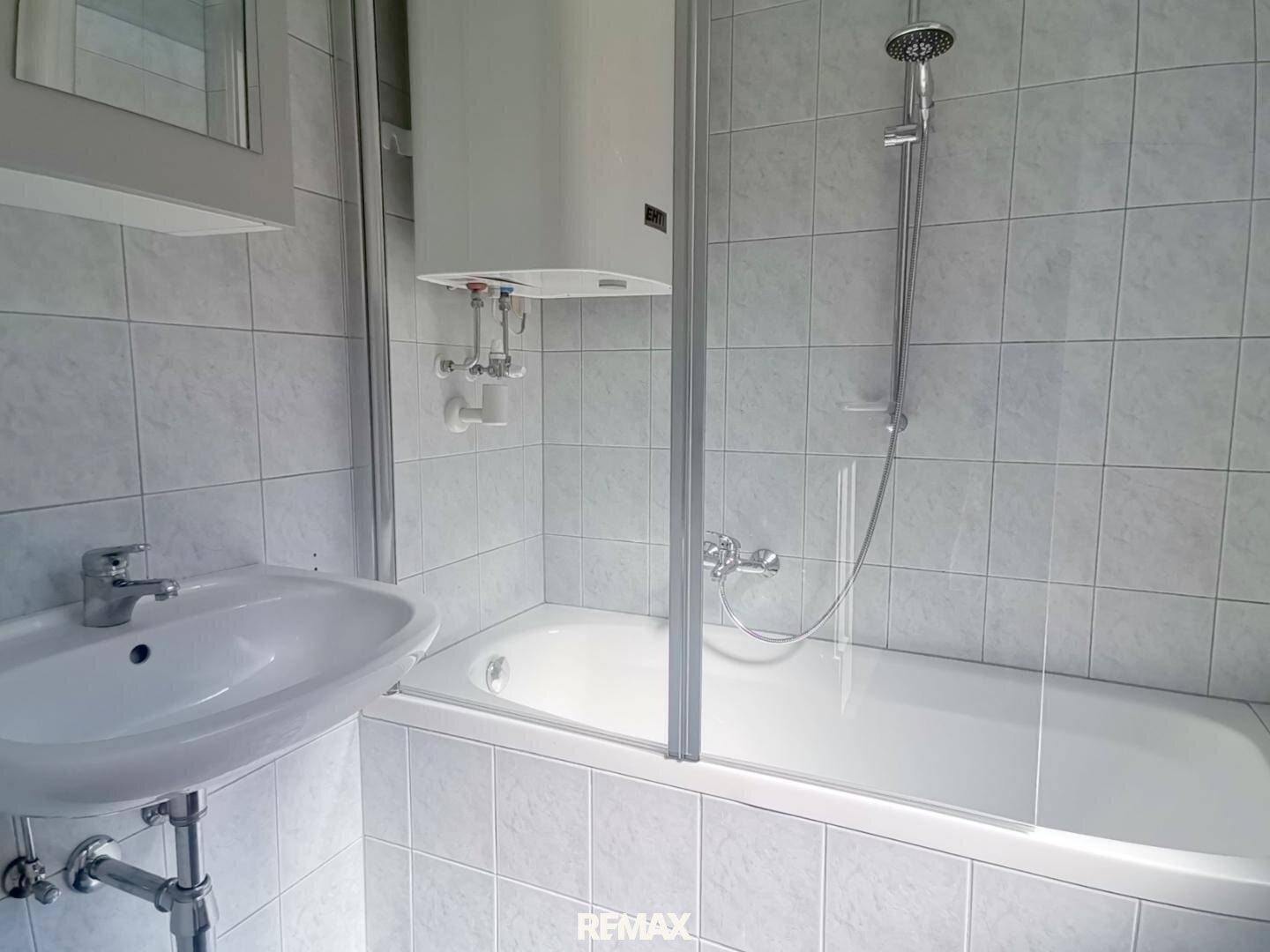 Funktionales Badezimmer mit Badewanne, Duschvorrichtung und hellen Fliesen an den Wänden.