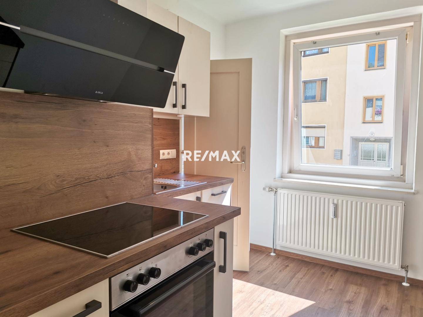 Moderne Küche mit Holzarbeitsplatten, Induktionskochfeld und Dunstabzugshaube, hell durch Fenster.