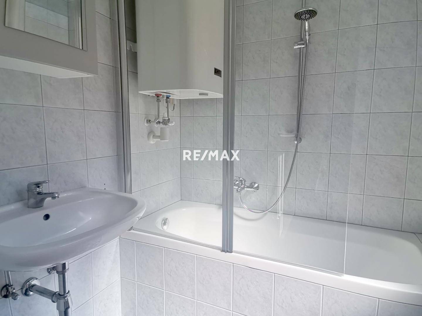 Funktionales Badezimmer mit Badewanne, Duschabtrennung und Waschbecken, komplett gefliest.