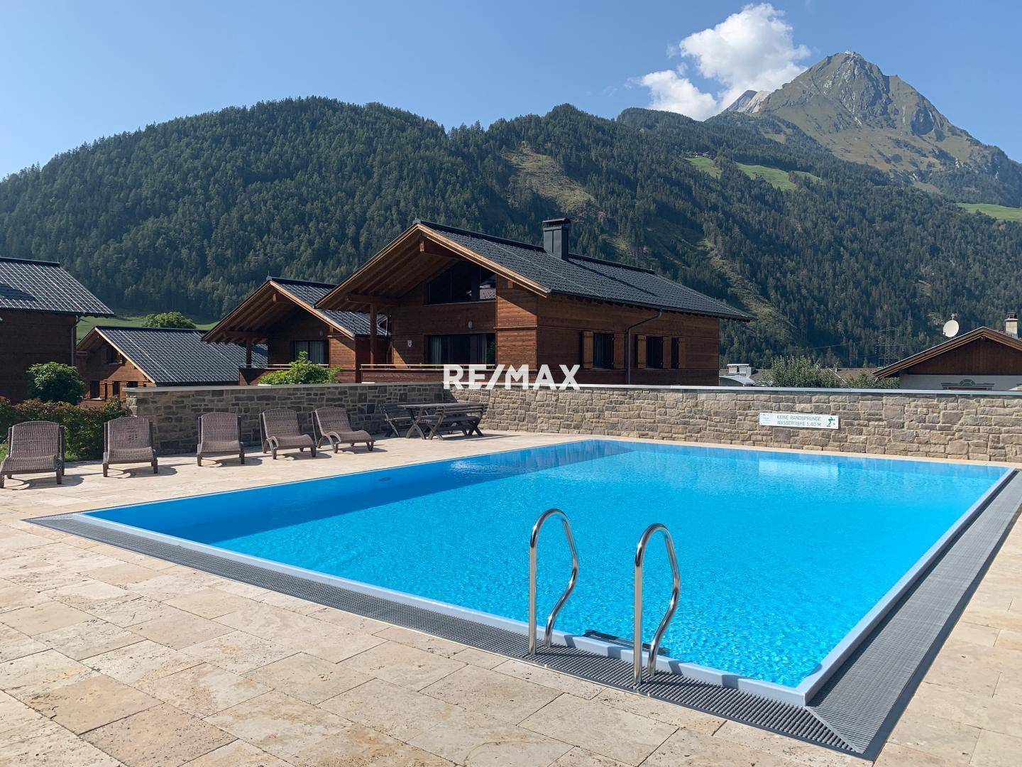 Großzügiger Außenpoolbereich mit gepflasterter Terrasse und Liegestühlen, umgeben von alpiner Bergkulisse.