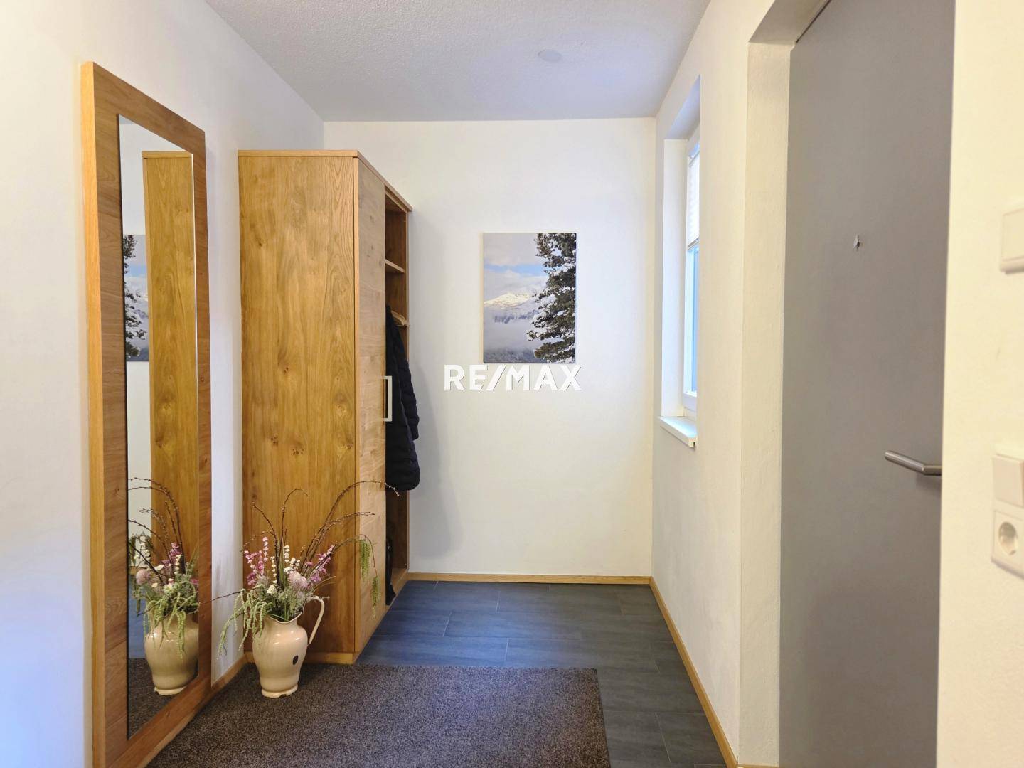 Heller Eingangsbereich mit Holzschrank, Spiegel und dunklem Fliesenboden, der einen einladenden Empfang bietet.