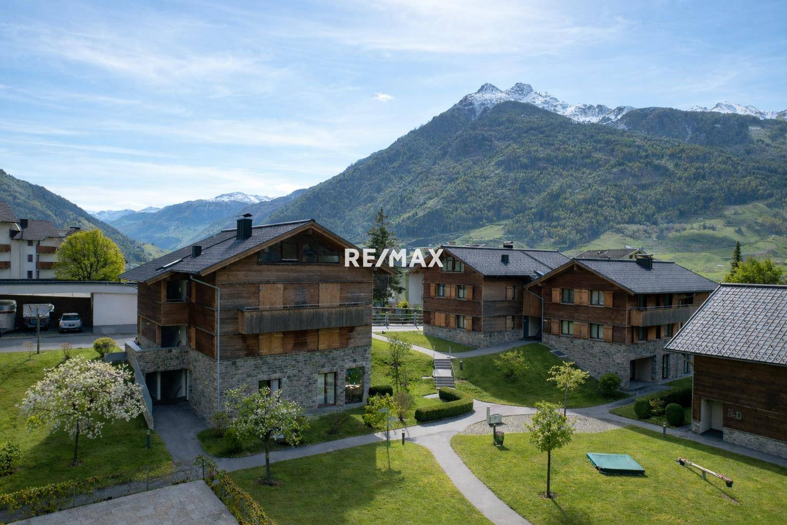 Weitläufige Außenanlage mit mehreren Gebäuden im alpinen Stil, gepflegten Grünflächen und beeindruckendem Bergpanorama.