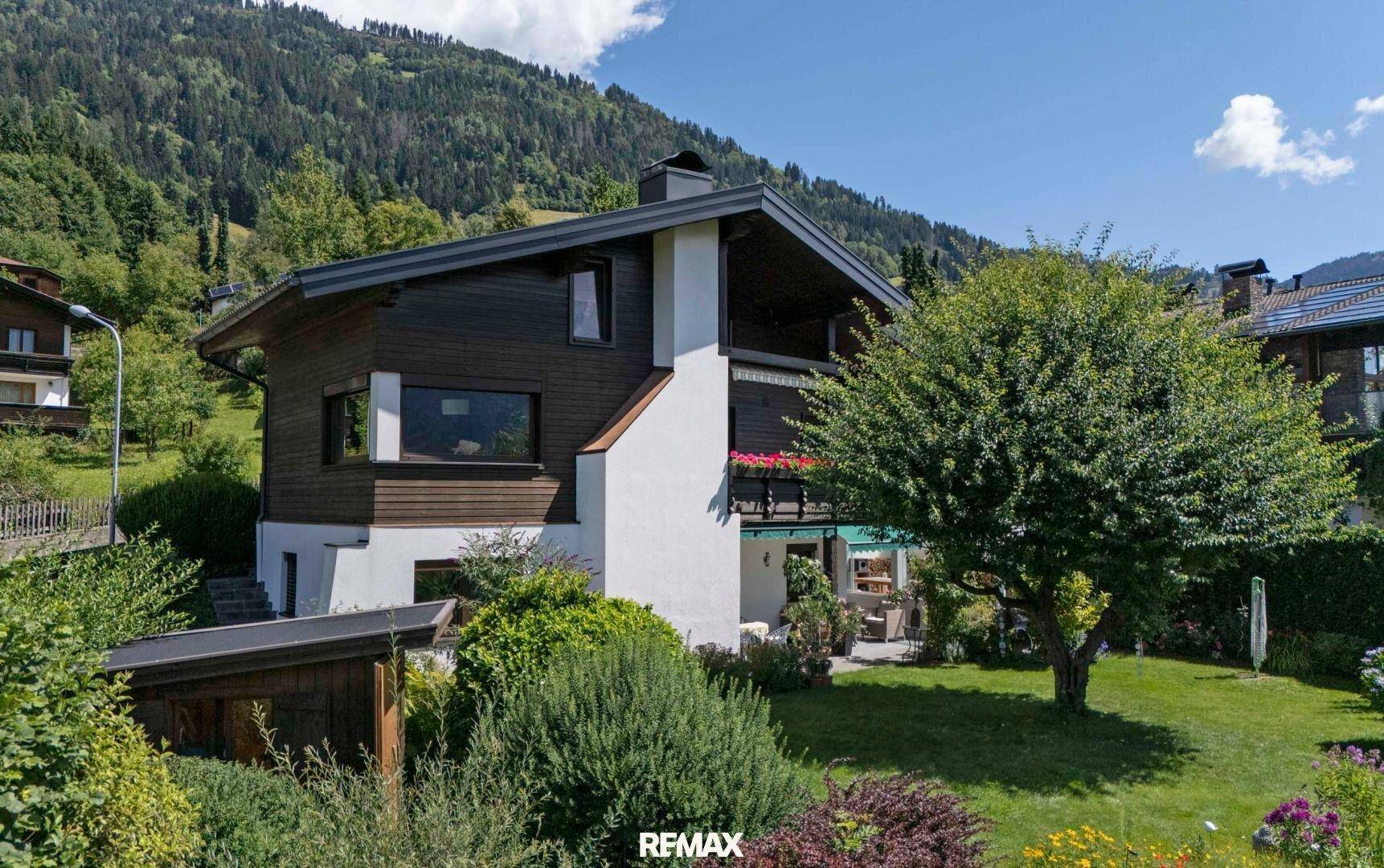 Charmantes Haus mit Holzfassade und gepflegtem Garten in bergiger Umgebung.