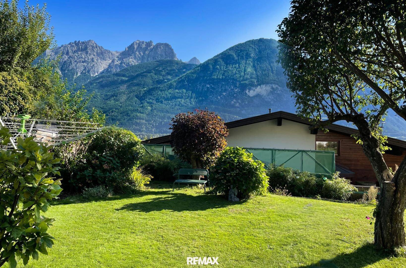 Ruhiger Garten mit grüner Rasenfläche, Sitzbank und beeindruckendem Bergblick im Hintergrund.