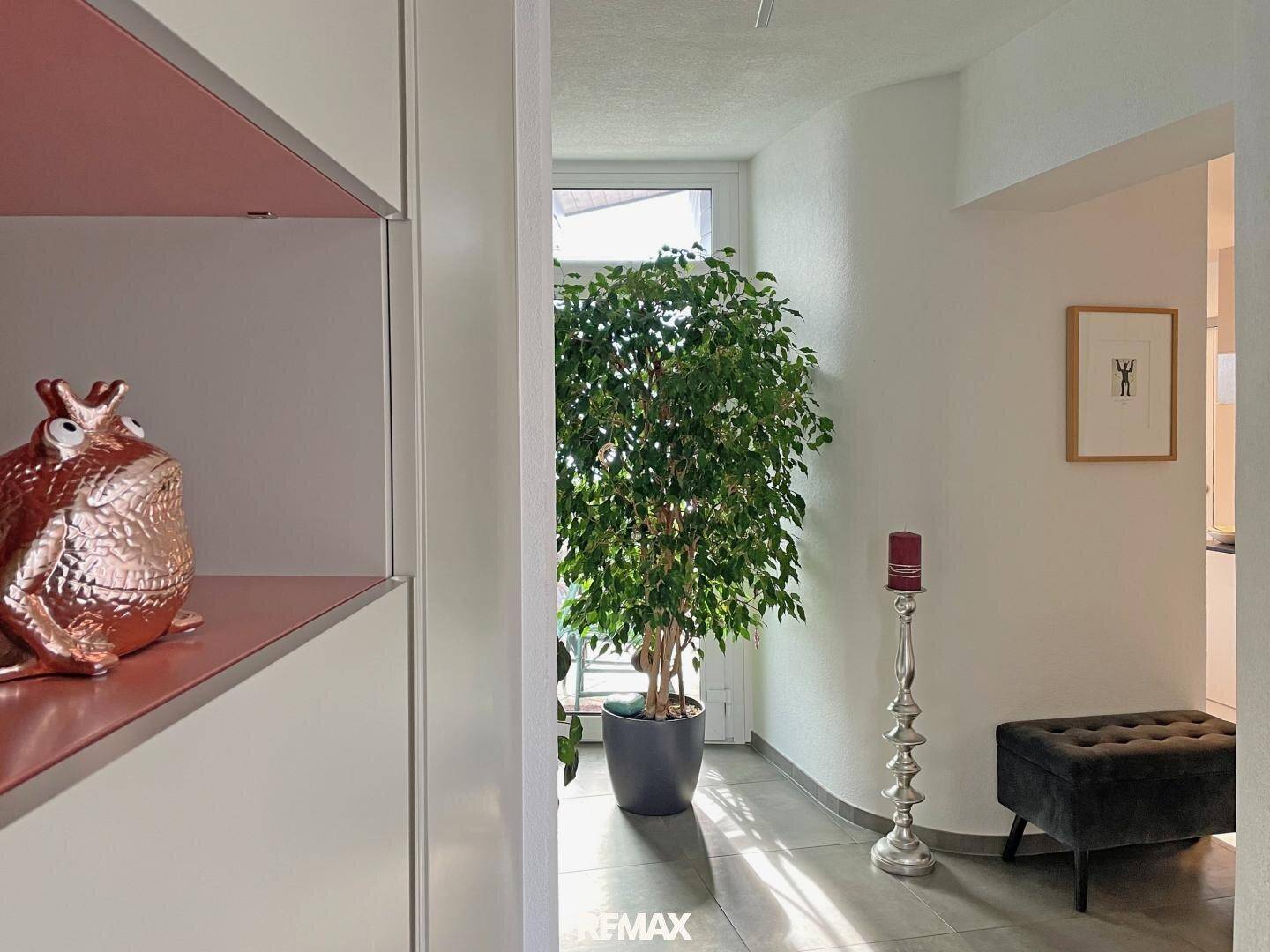 Heller Eingangsbereich mit großem Fenster, Grünpflanze und moderner Dekoration.