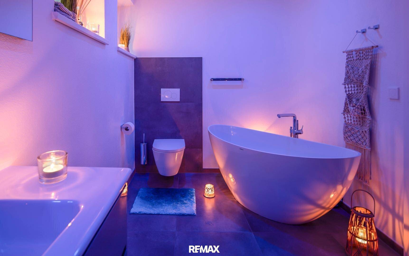 Badezimmer mit freistehender Badewanne und stimmungsvoller violetter Beleuchtung.