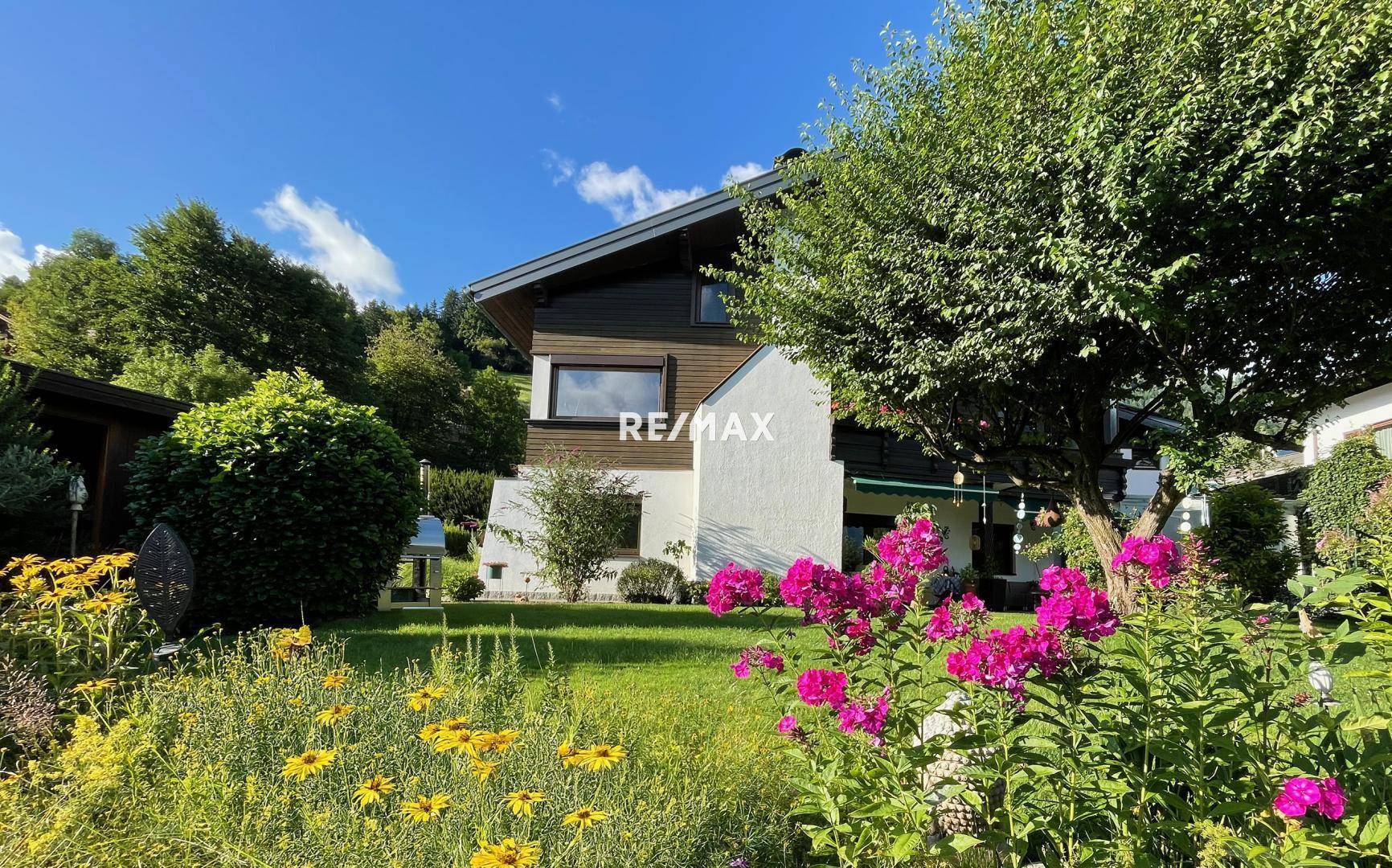 Sonniger Gartenbereich mit üppiger Vegetation und Blick auf die moderne Architektur des Hauses.