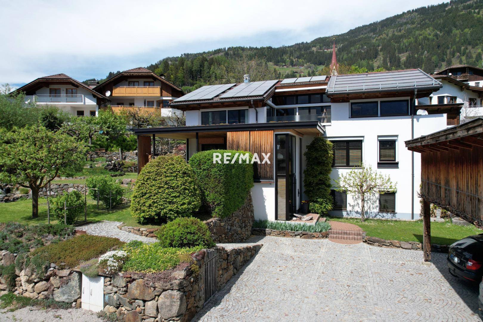 Modernes Wohnhaus mit Photovoltaikanlage auf dem Dach und gepflasterter Auffahrt in bergiger Umgebung.