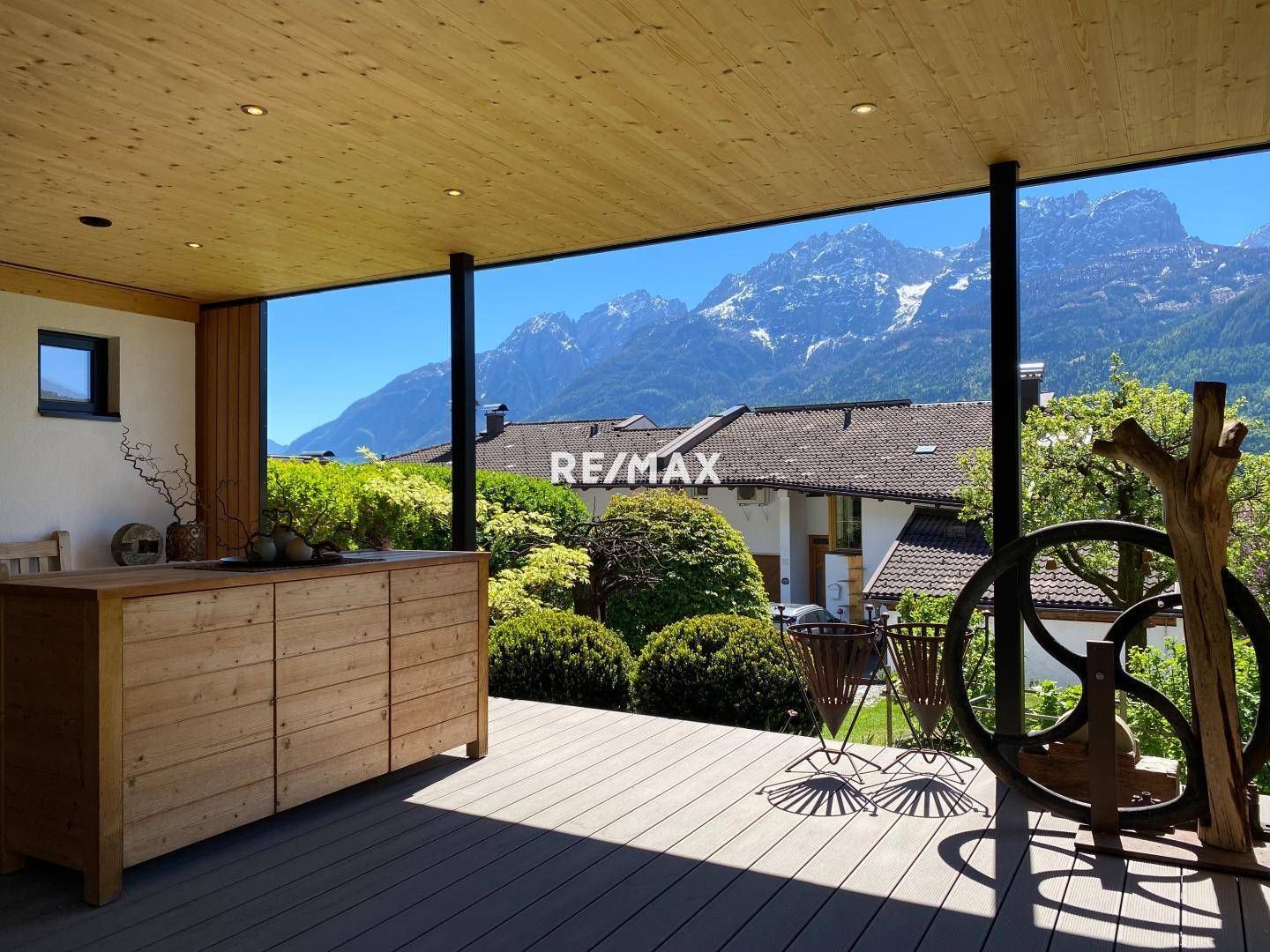 Überdachte Terrasse mit Holzboden, Außenküchenelement und beeindruckendem Bergblick.