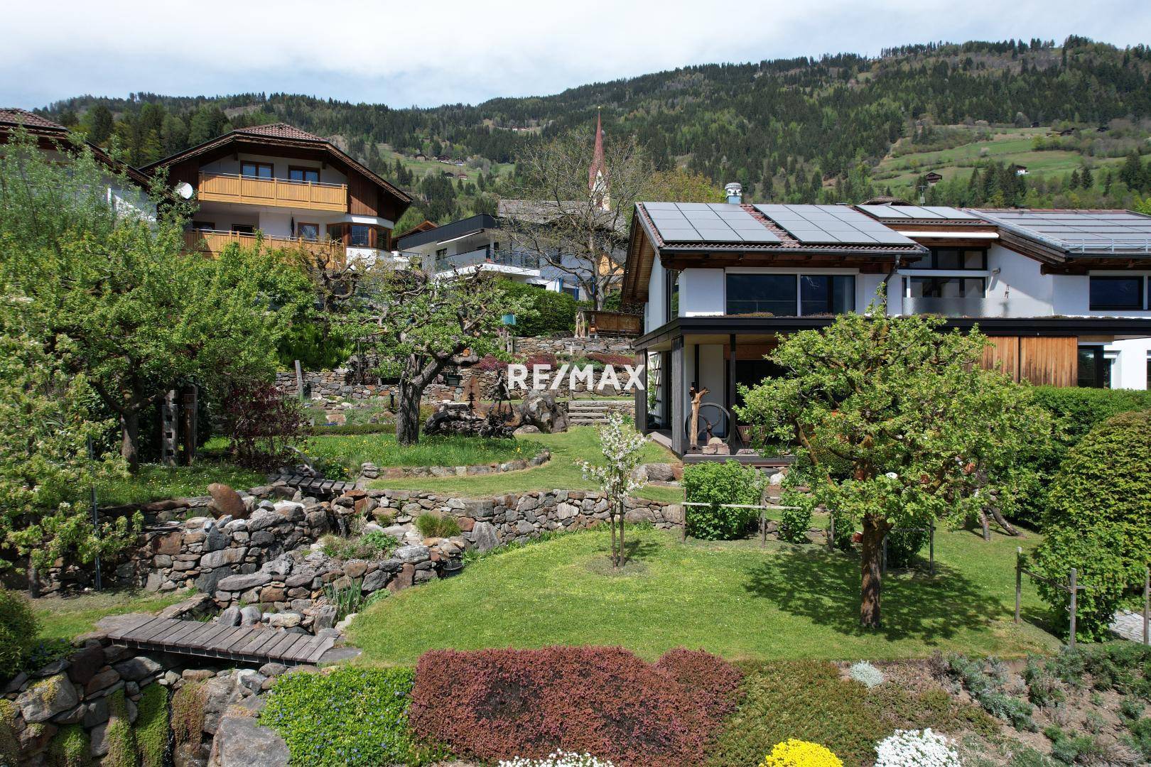 Großzügiger Gartenbereich mit Terrassen, Steinmauern und Photovoltaikanlage auf dem Hausdach.