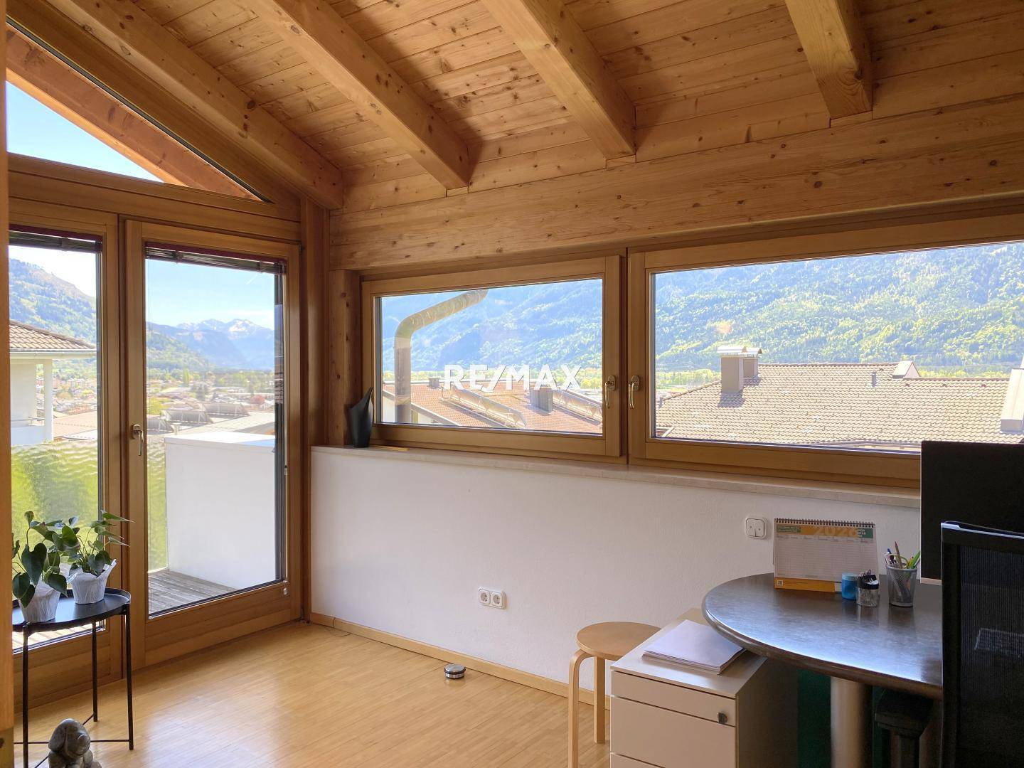 Arbeitszimmer mit Holzbalkendecke, großen Fenstern und weitem Blick auf die Berge.