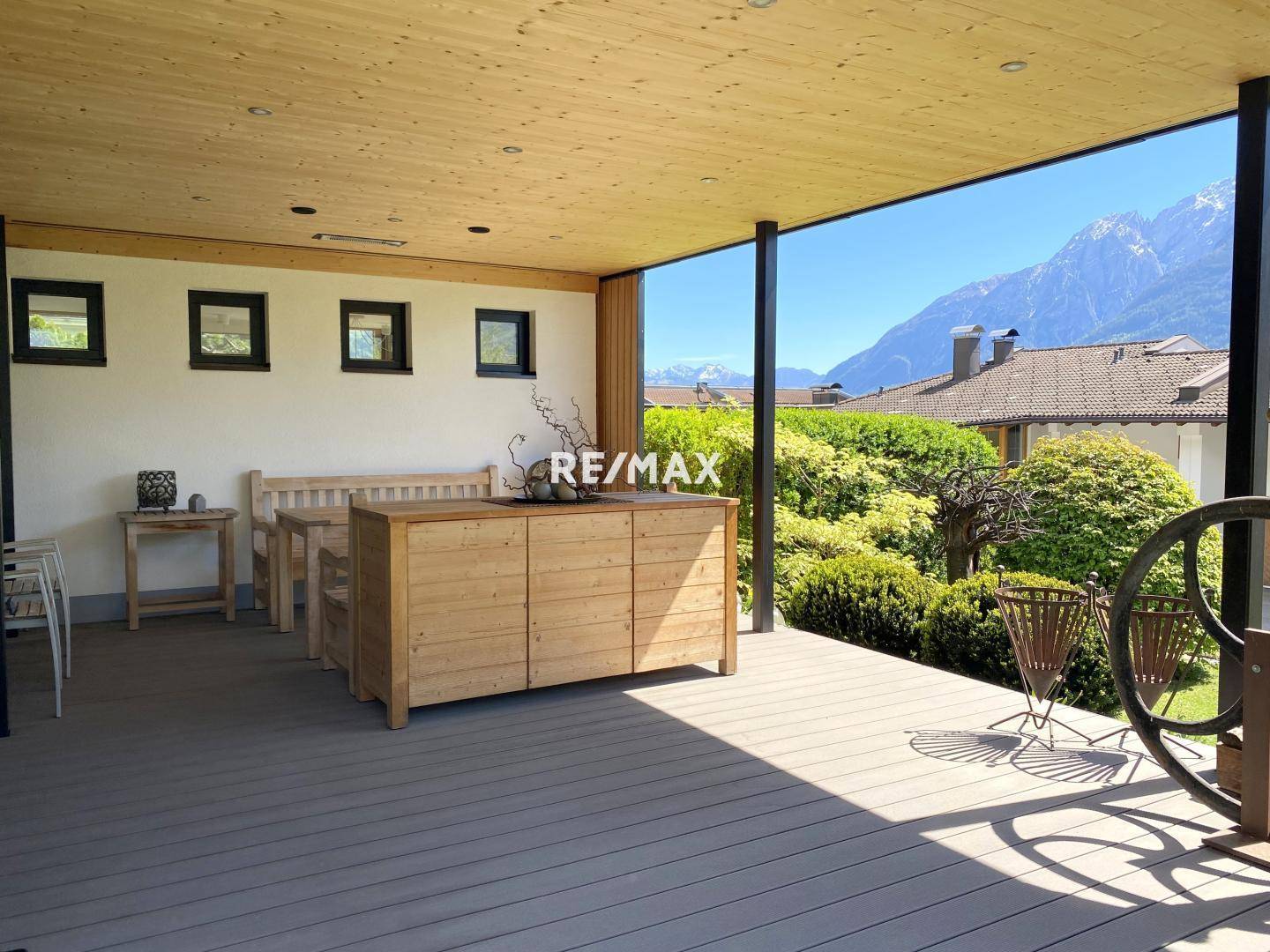 Große überdachte Terrasse mit Holzboden, Sitzgelegenheiten und weitem Blick auf die Alpen.