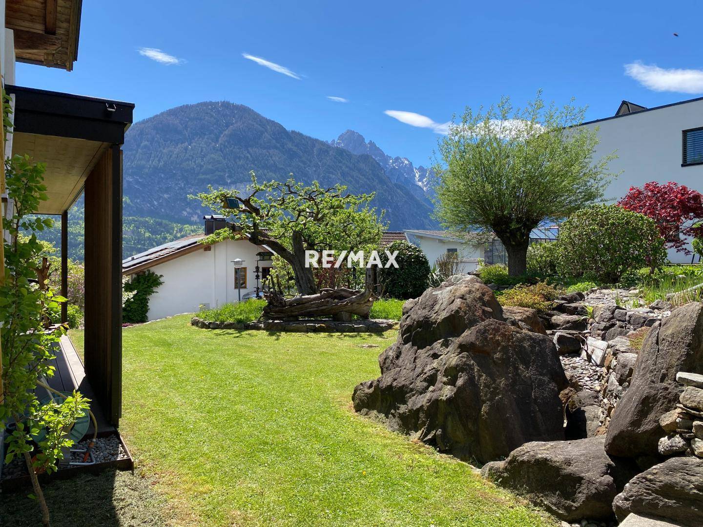 Gepflegter Garten mit Rasenfläche, großen Felsen und Blick auf die umliegende Natur.