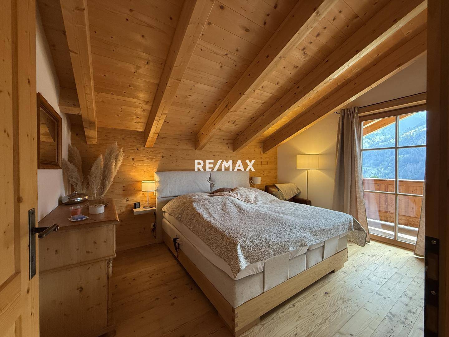 Helles Schlafzimmer mit Holzbalkendecke, Holzboden und großem Fenster mit Bergblick.