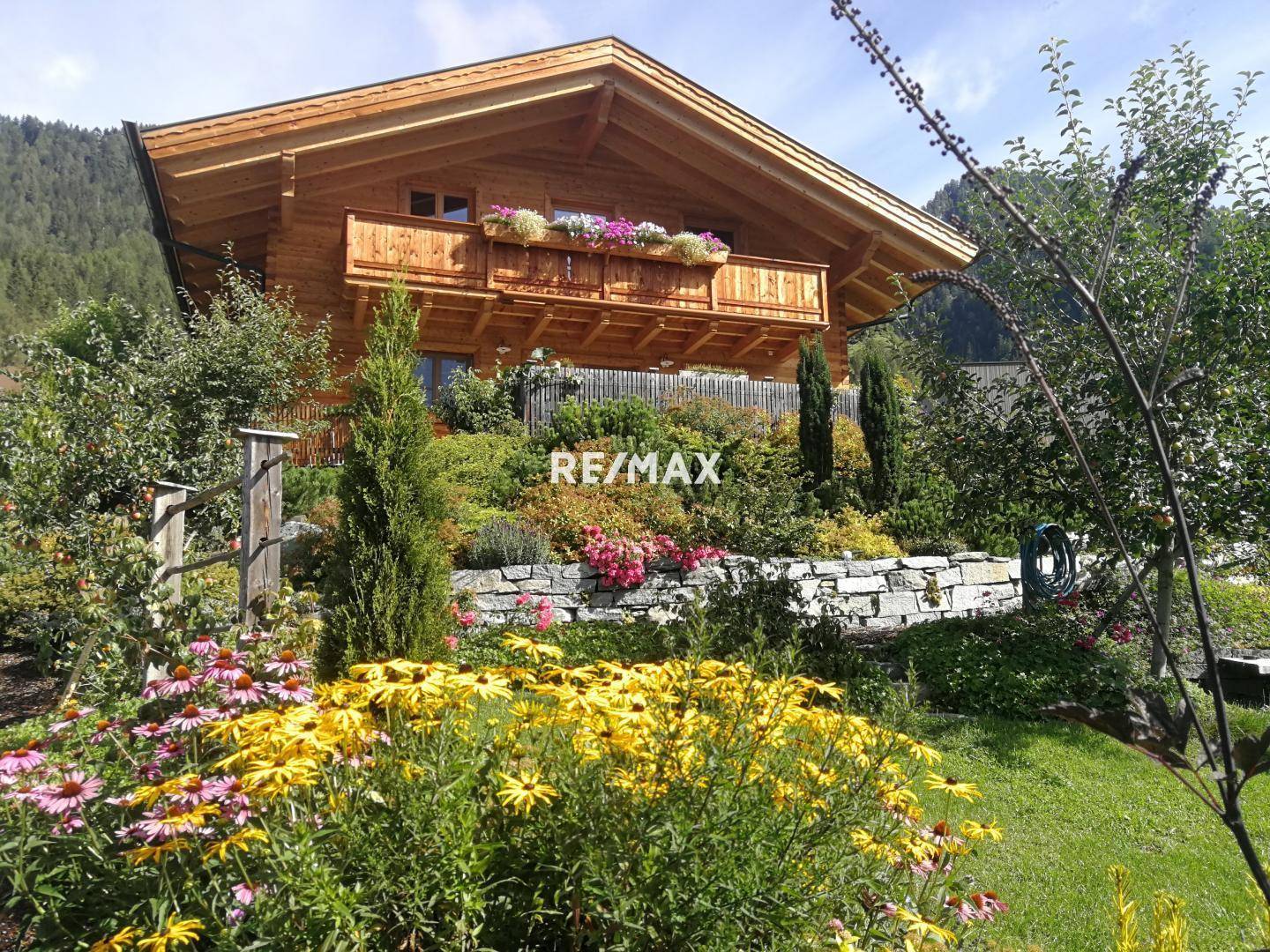 Charmantes Holzhaus umgeben von einem farbenprächtigen, blühenden Garten mit Steinmauer.