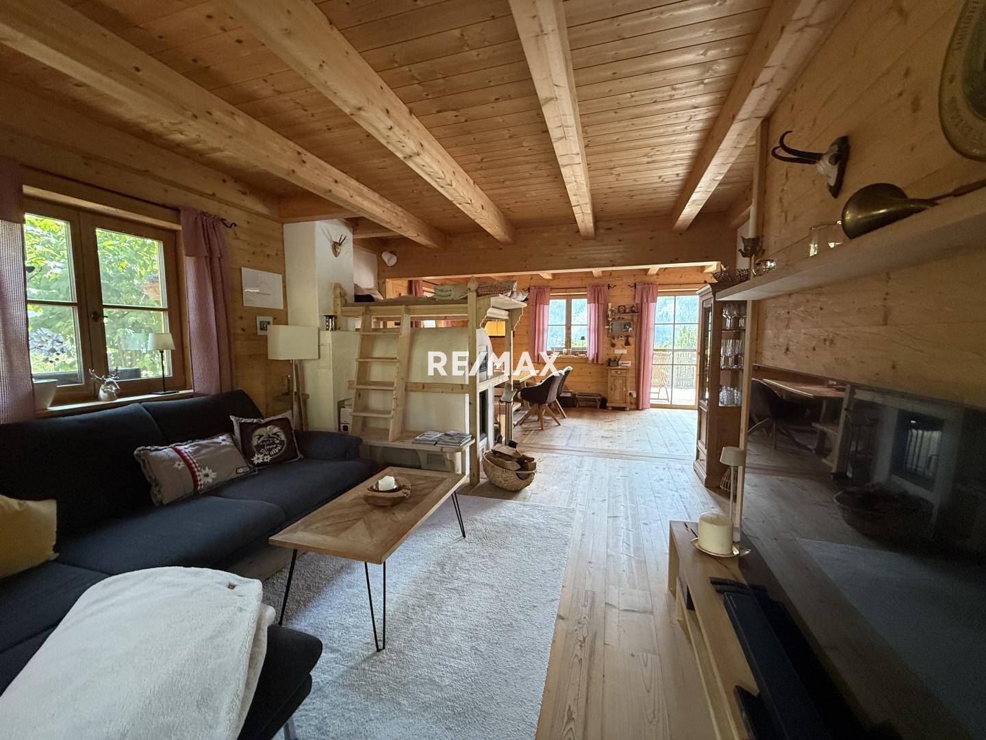 Geräumiges Wohnzimmer mit Holzbalkendecke, Kamin und Zugang zum Balkon, im alpinen Stil.