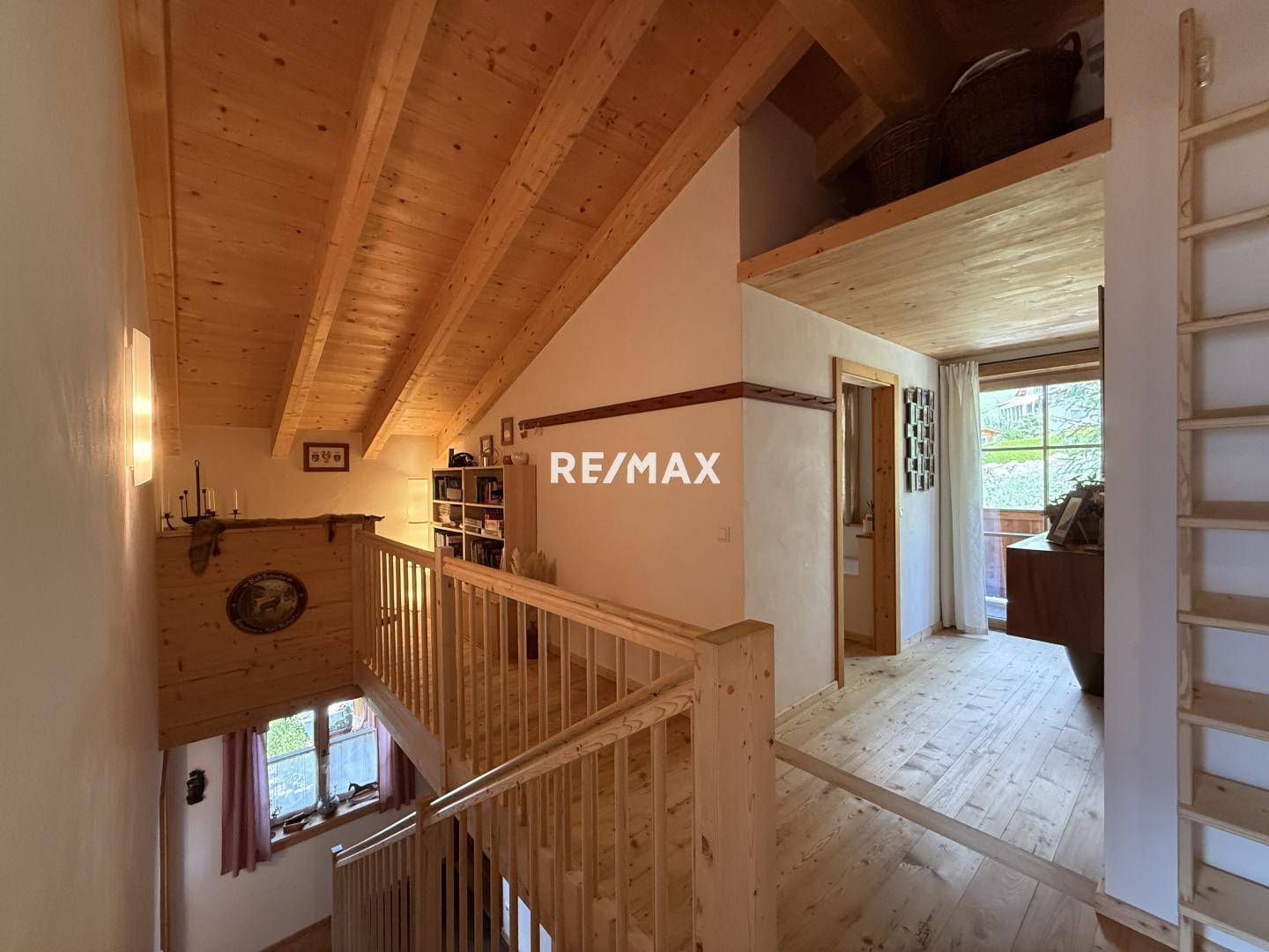 Offener Galeriebereich mit Holzgeländer und Blick auf die untere Etage, mit Holzbalkendecke.